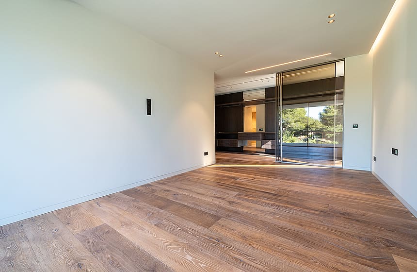 Empty interior room with wide-plank oak flooring and recessed ceiling lighting leading to a terrace with garden views.