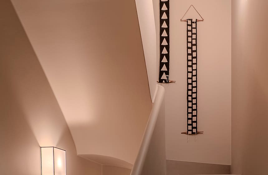 Modern staircase with smooth plaster walls, warm wall sconces, and vertical geometric wall art.
