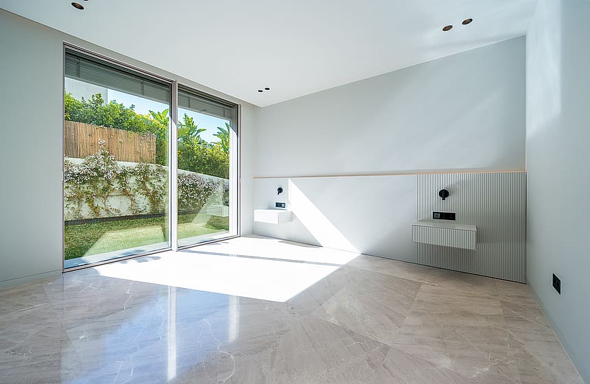 A modern bathroom featuring polished stone flooring, two floating vanity basins, and large sliding glass doors opening to a garden.