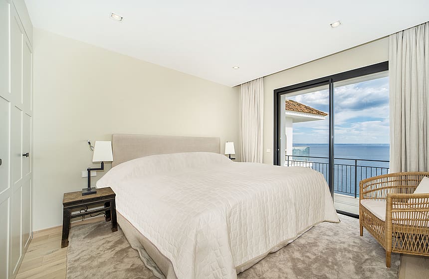 A master bedroom featuring a large bed, built-in wardrobes, and sliding glass doors opening to a terrace with ocean views.
