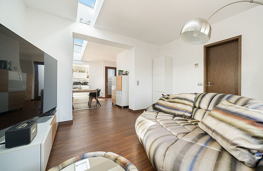 Modern living room with a large curved sofa, wooden floors, and natural light from a ceiling skylight.
