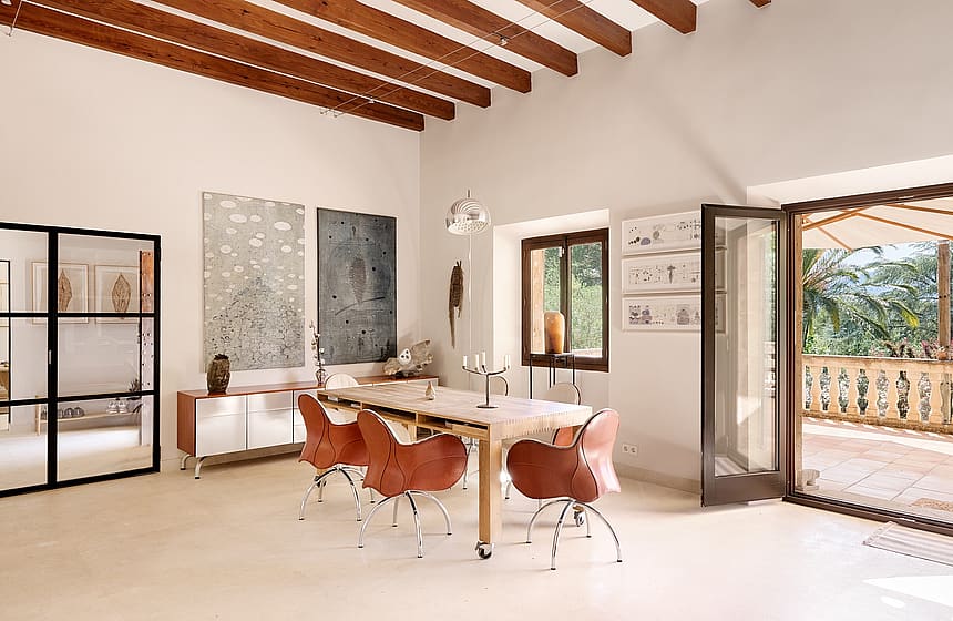 Dining room in a Finca featuring a long wooden table, leather swivel chairs, exposed ceiling beams, and a terrace doorway.