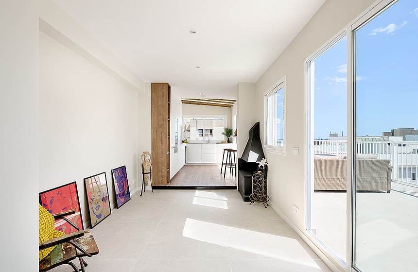 Bright living area with white walls, tile floors, and a corner fireplace, leading to an outdoor terrace with sea views.