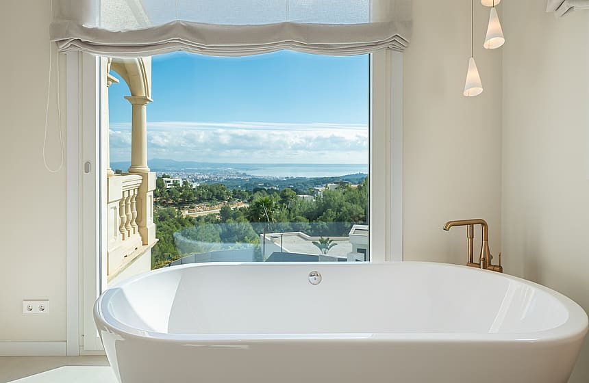 A white freestanding bathtub positioned in front of a large window with views of the coastline and Mediterranean Sea.