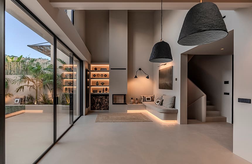 Minimalist living room featuring a tall fireplace, woven pendant lights, and large glass doors opening to a private patio.
