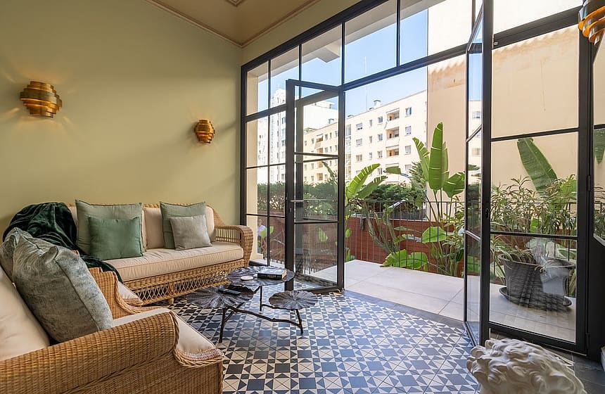 Sunroom featuring a wicker sofa, patterned ceramic floor tiles, and black-framed glass doors opening to a private patio.