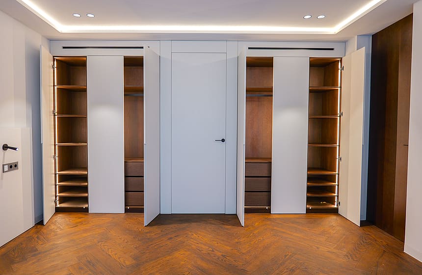 A floor-to-ceiling built-in wardrobe with white doors and wooden interior shelving, featuring integrated LED accent lighting.