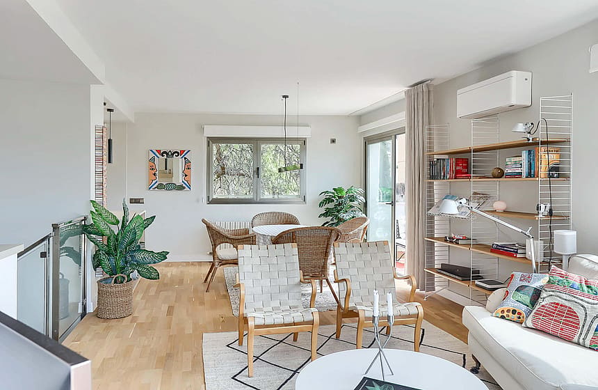 An open living room and dining space with light wood flooring, contemporary furniture, a patterned rug, and potted plants.