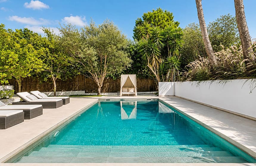 Rectangular swimming pool with tiled interior, sun loungers and canopy daybed surrounded by mature Mediterranean planting