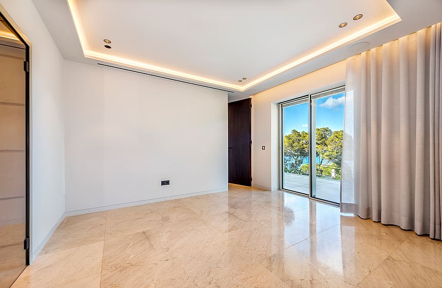 Empty modern bedroom with polished light marble floor, recessed ceiling lighting, and sliding glass doors to a balcony.