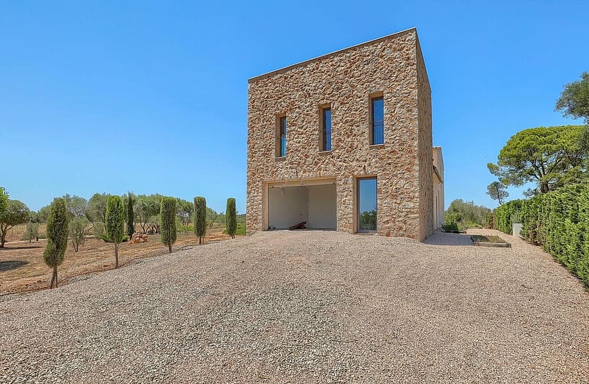 Two-story stone-clad outbuilding with narrow windows and an open ground-level portico, set against a gravel driveway.