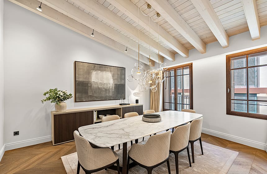 Contemporary dining room featuring a white marble table, upholstered chairs, and exposed white-washed ceiling beams.