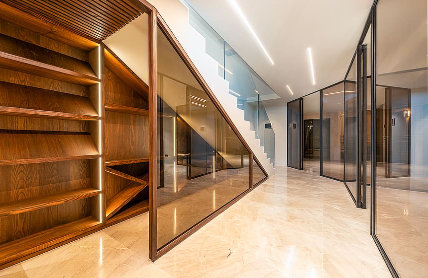 Interior hallway featuring polished marble floors, a glass staircase partition, and integrated wooden shelving units with linear lighting.