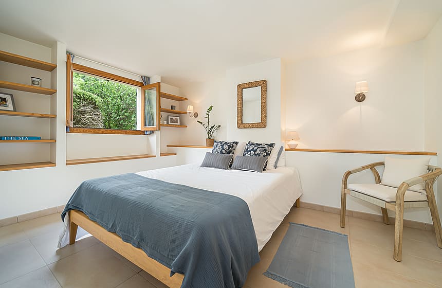Bright bedroom featuring a wooden bed frame, custom oak shelves, and a window overlooking a lush garden wall.