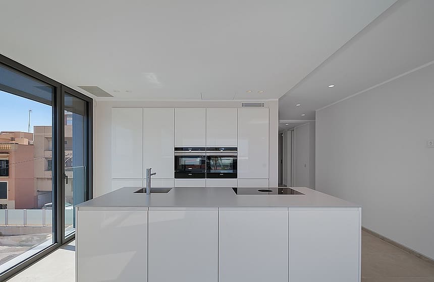 Integrated white kitchen and living area with large sliding glass doors opening to terrace and sea view