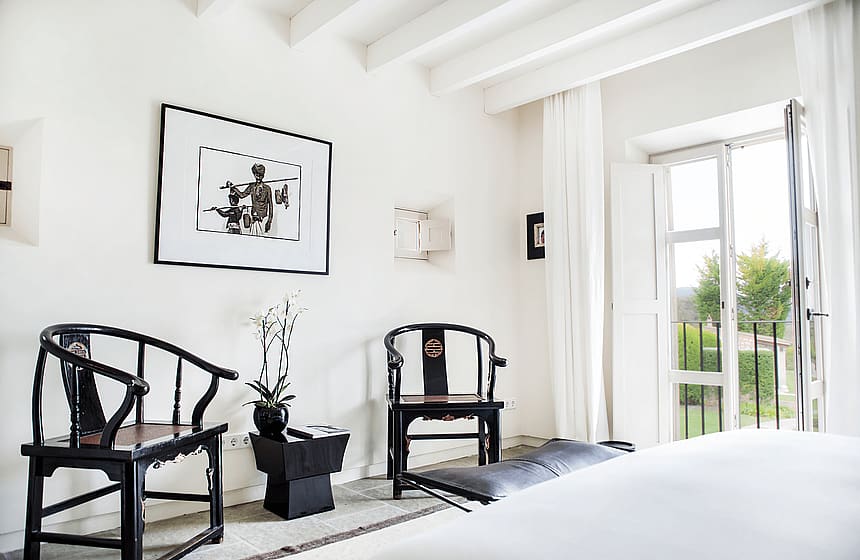 A bright living space with white walls, beamed ceilings, and two dark wooden antique Chinese-style chairs flanking a side table.