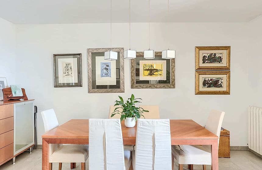 Dining area featuring a rectangular wooden table, four white upholstered chairs, and a gallery wall with framed prints.