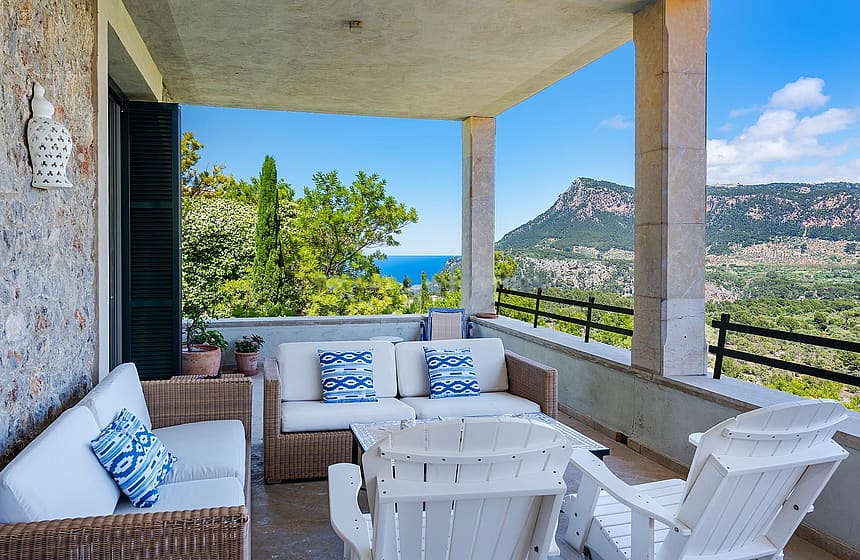 Large covered terrace with fireplace, multiple seating zones, and uninterrupted view across forested valley to distant mountains