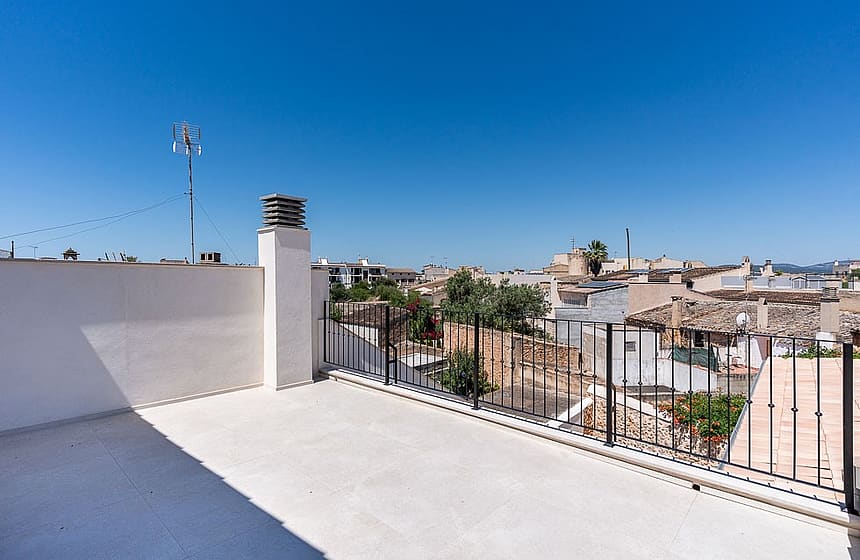 An open, paved rooftop terrace with white walls and a black metal railing overlooking the traditional tiled roofs of Campos.