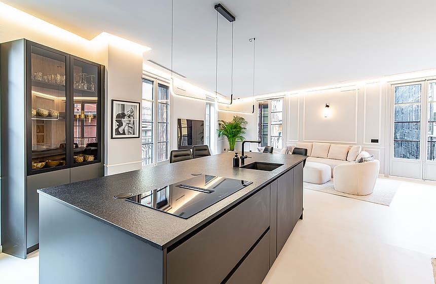 Modern open-plan kitchen with a large dark charcoal island, integrated appliances, and recessed lighting, overlooking a bright living area.