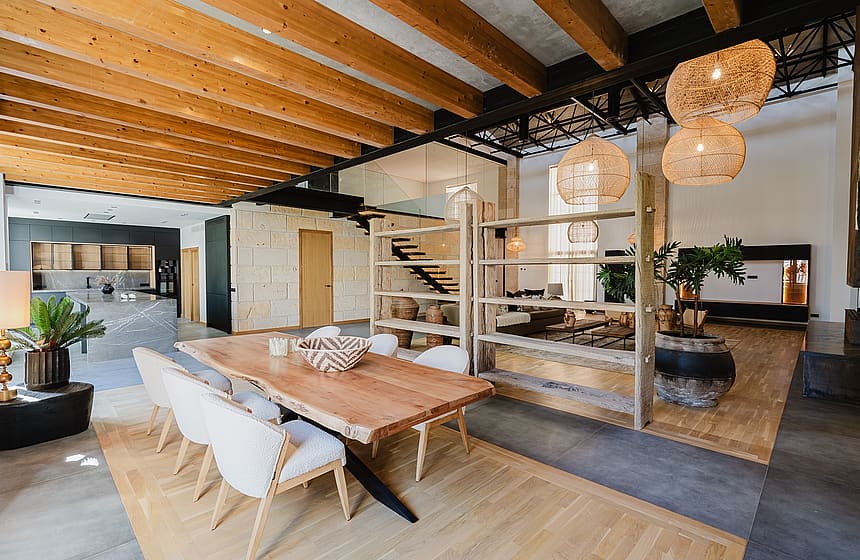 Dining room with a live-edge wooden table, wicker pendant lights, and exposed wooden ceiling beams in a loft-style apartment.