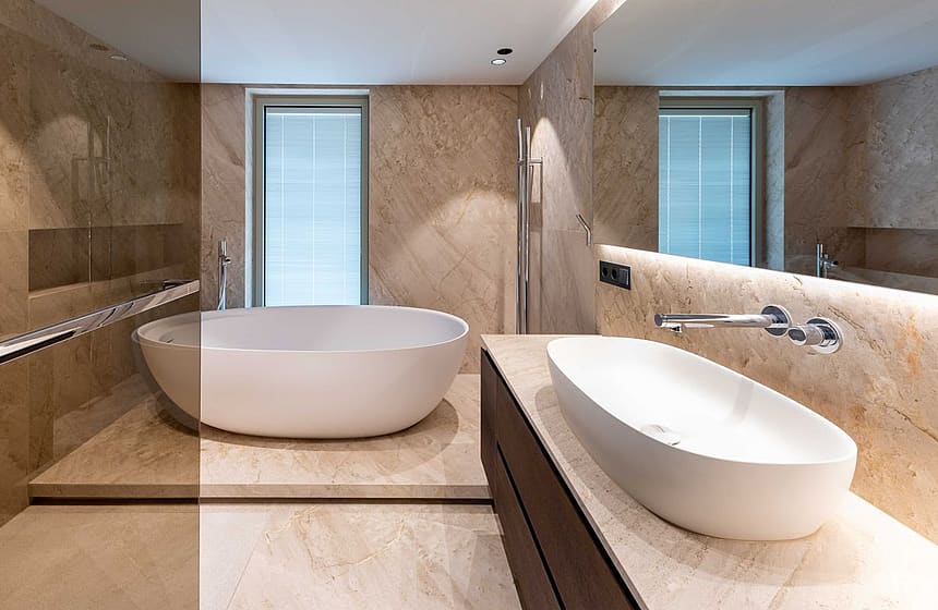 Modern bathroom featuring a freestanding white oval bathtub, dark wood vanity, and beige travertine tile walls.