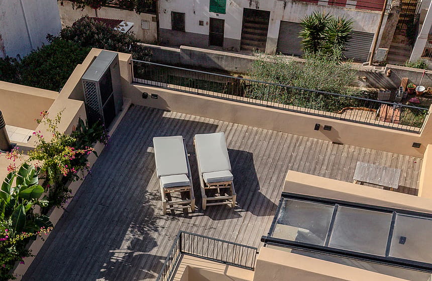 Aerial view of a townhouse rooftop terrace with wooden decking, two sun loungers, and a glass skylight section.