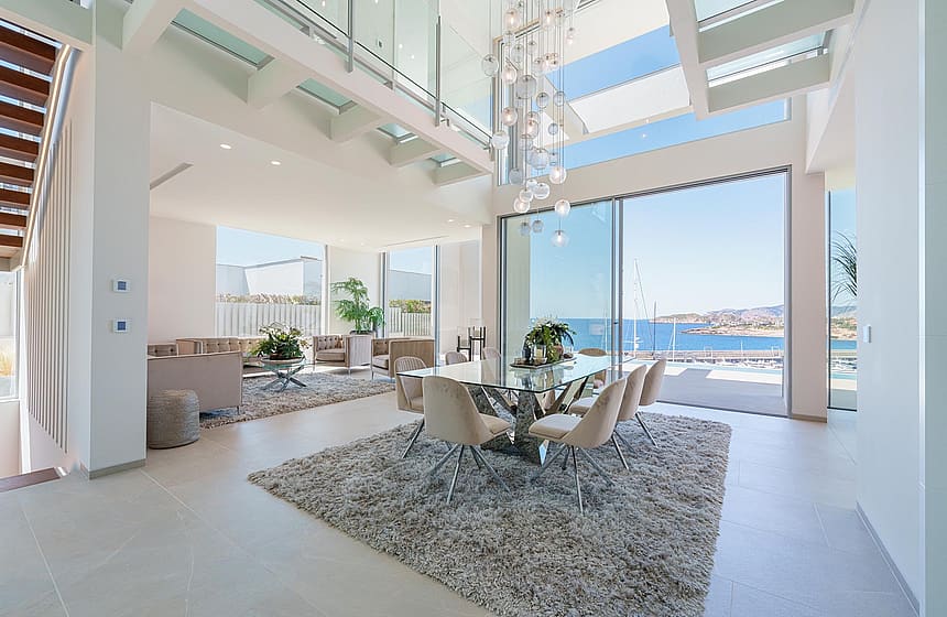 Double-height living and dining space with floor-to-ceiling sliding glass doors opening to a coastal view.