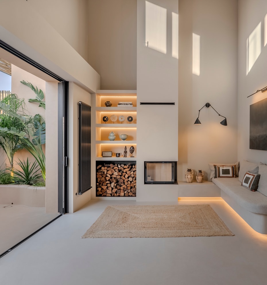 Double-height living area featuring a built-in sofa, modern fireplace, and glass doors opening to a tropical patio.