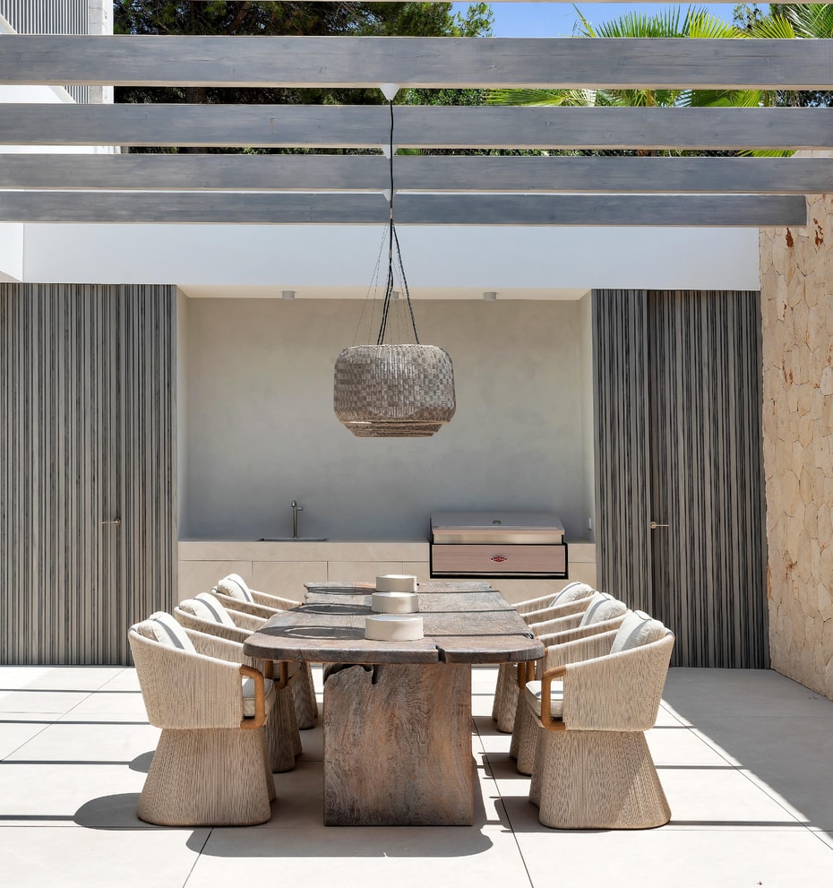 Covered outdoor dining area with exposed beam pergola, Mallorcan stone wall and wicker pendant lights