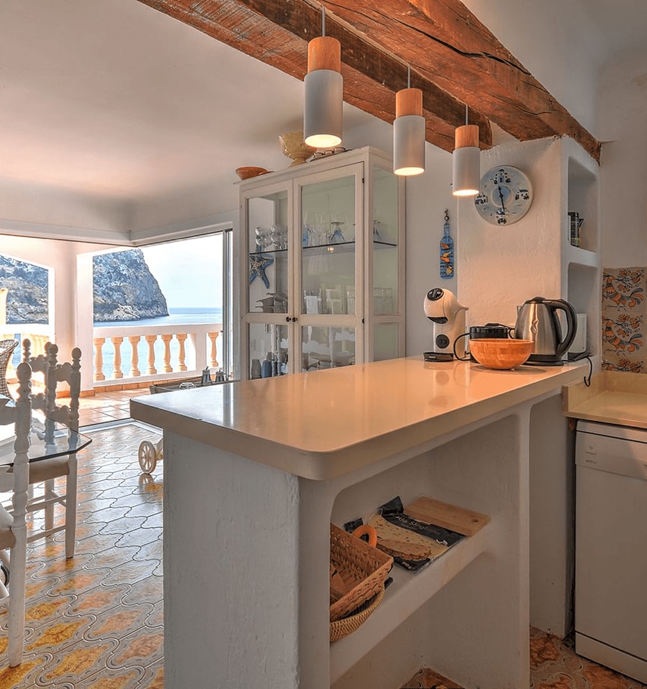 Kitchen and dining area with white cabinets, patterned tiled floor, and views of the Mediterranean coastline.