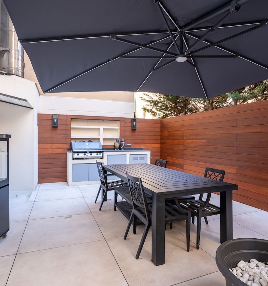 A private outdoor terrace in Palma featuring a dining table, black chairs, a large charcoal umbrella, and a built-in grill.