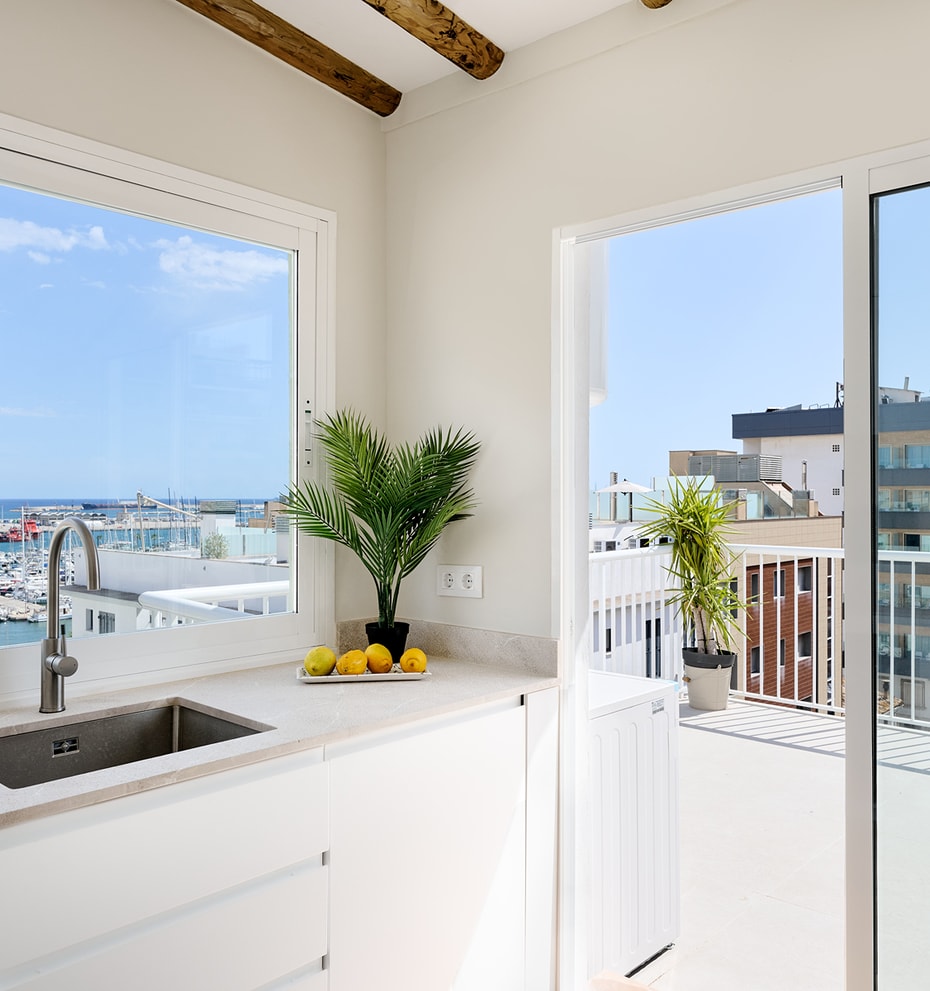 Modern kitchen corner with white cabinets and stone countertop, featuring large sliding glass doors opening to a balcony.