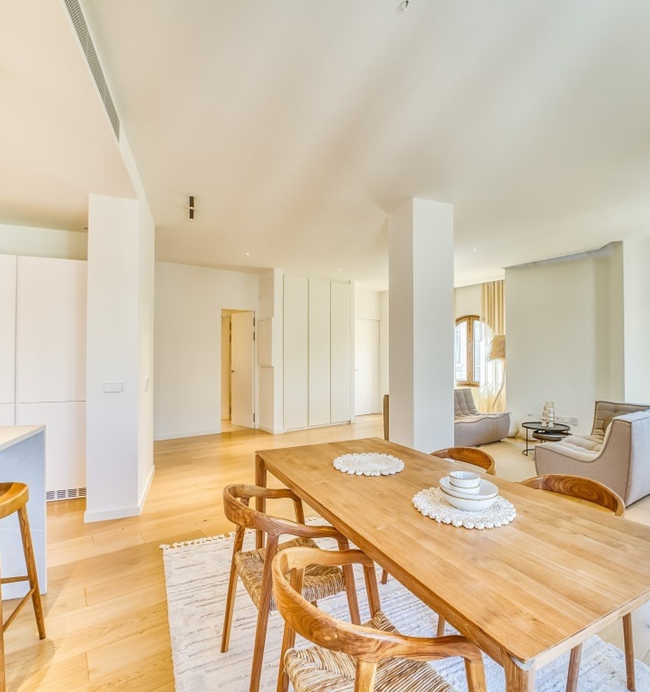 Open-plan room featuring a light wood dining table with curved wooden chairs and a minimalist kitchen island with bar stools.