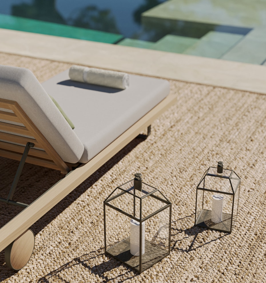 Close-up of a wooden sun lounger with cream cushions beside a pool, with two decorative metal lanterns on a gravel terrace.