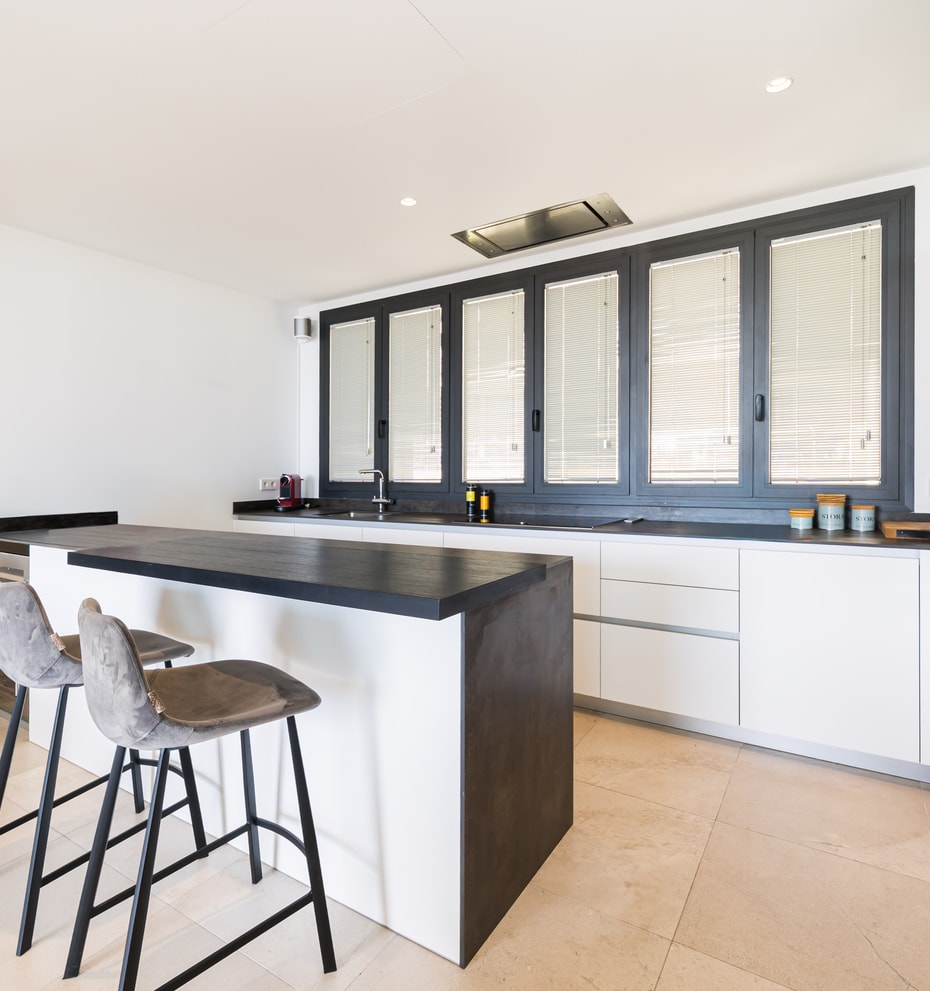 A minimalist kitchen featuring white handleless cabinetry, a dark grey island, and large dark-framed windows.