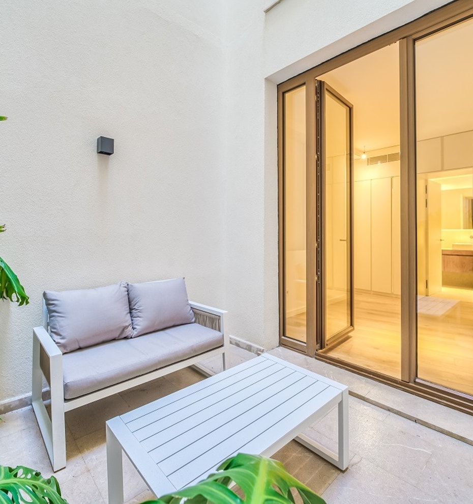 A small outdoor terrace with a two-seater sofa and coffee table next to large glass doors leading into an interior room.