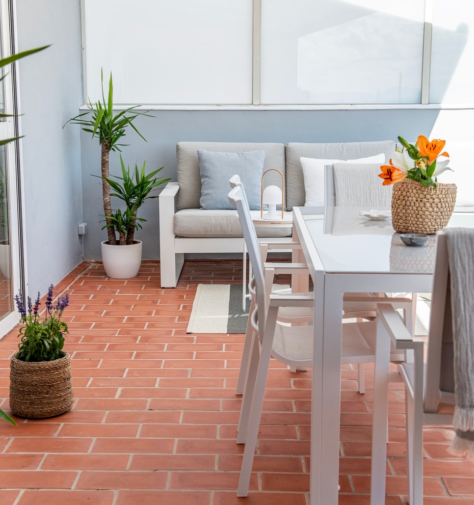 An outdoor terrace with terracotta tile flooring, a white dining table with matching chairs, and potted yucca plants.