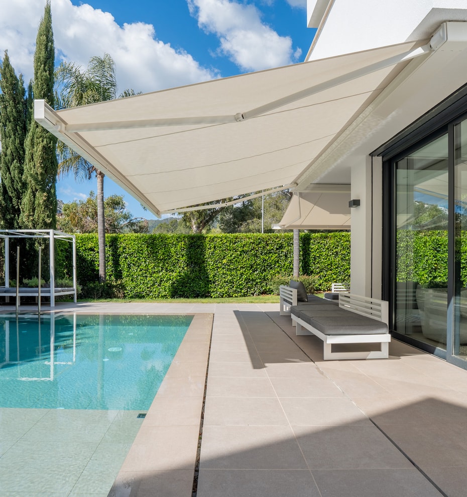 Heated saltwater swimming pool with sun loungers, retractable awning and tall hedge screening.