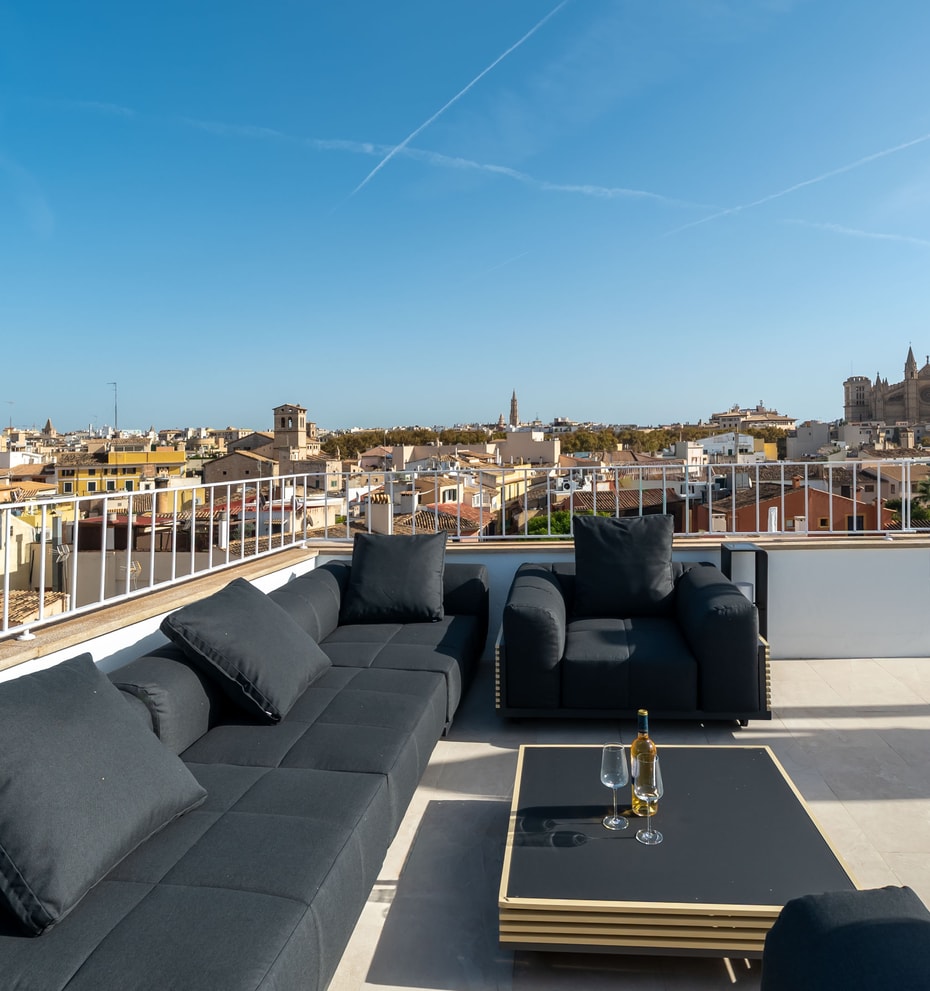 Modern black lounge furniture on a sun-drenched rooftop terrace overlooking Palma Old Town and the Cathedral.