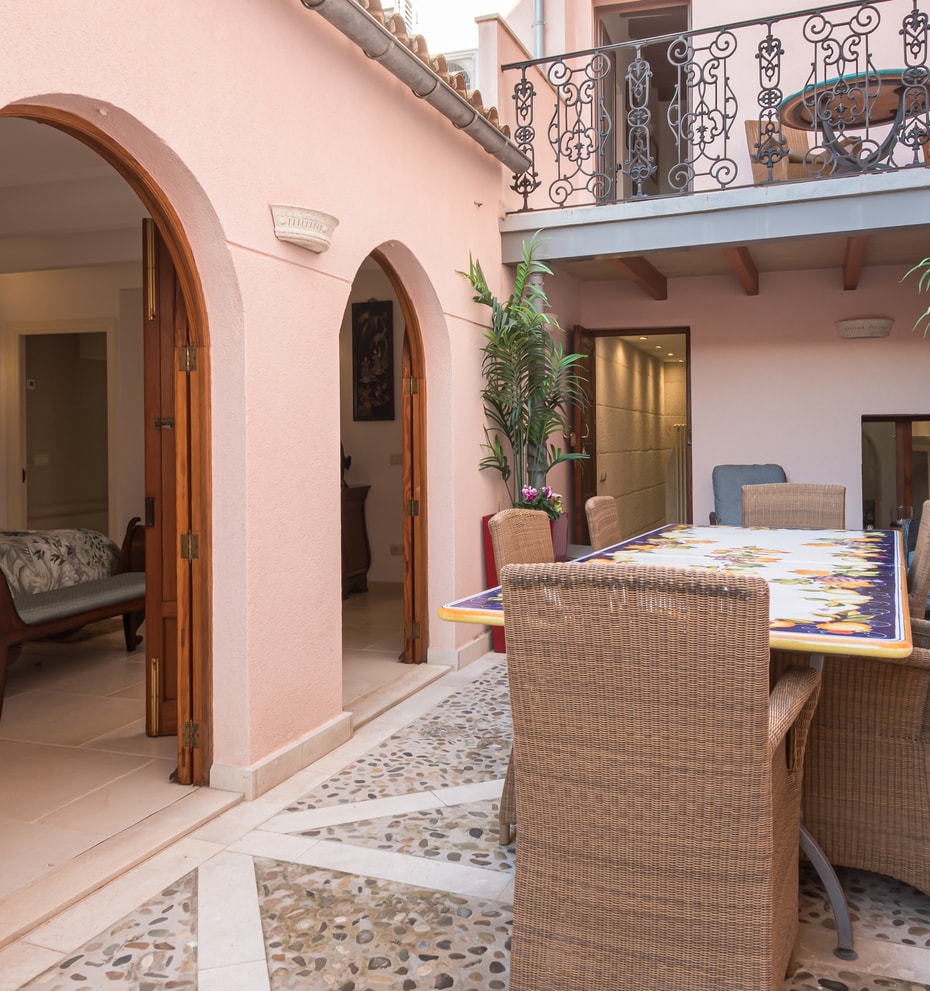 Pink-walled courtyard patio with a tiled dining table, potted plants and arched doorways