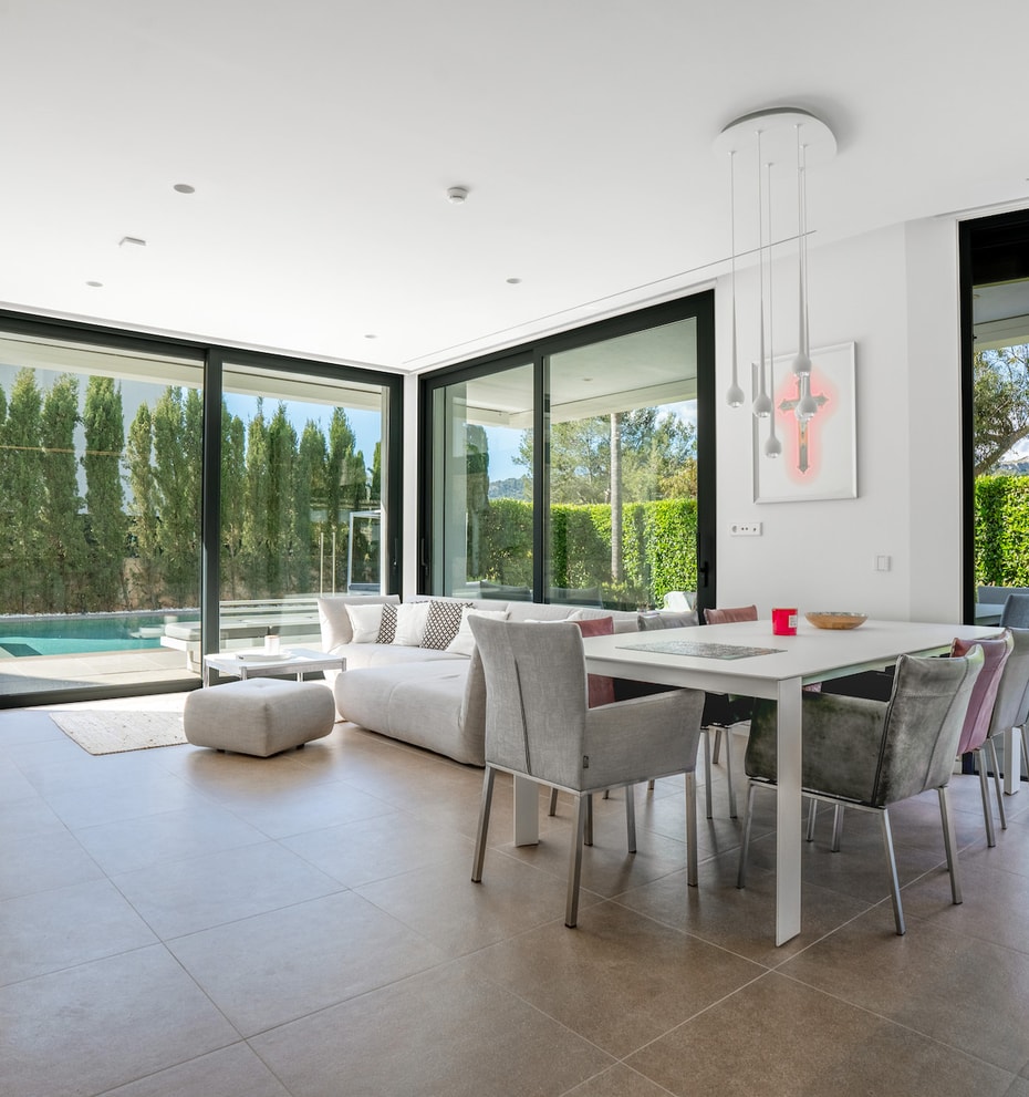 Open-plan living and dining room with corner sliding glass walls opening to the pool terrace and garden.