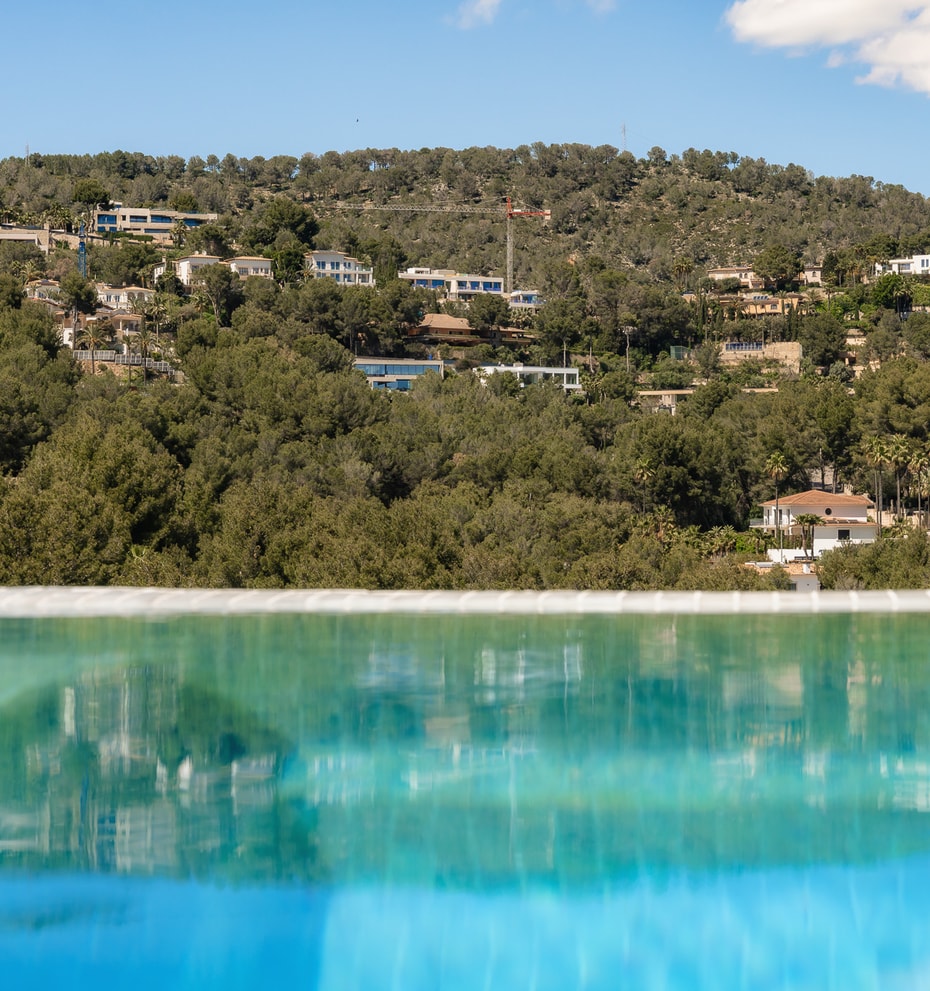 Close-up of an infinity pool edge reflecting the lush green hillside and villas of Son Vida under a clear sky.