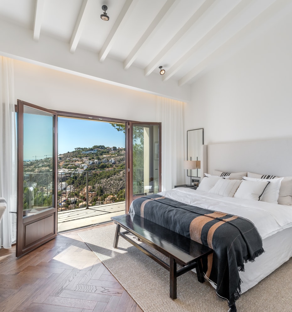 Bright bedroom with herringbone wood floors and open French doors leading to a terrace with sweeping valley views.