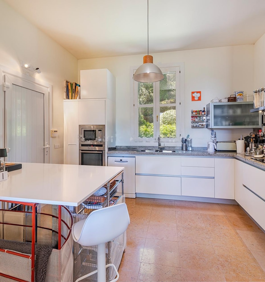Contemporary white kitchen with stainless-steel appliances, island workstation, and glass doors opening to terrace