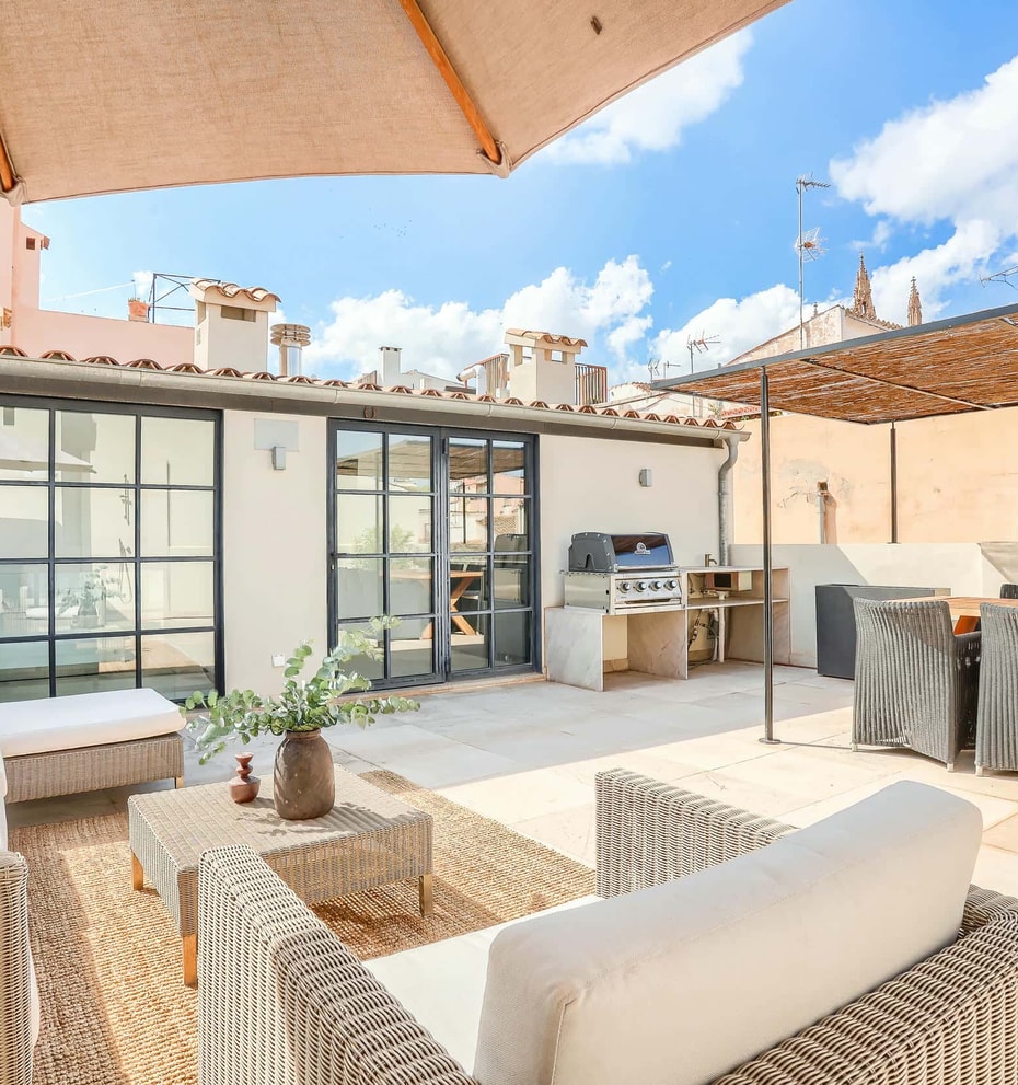 A spacious rooftop terrace in an Old Town townhouse features wicker seating, a dining area, and a built-in outdoor kitchen.