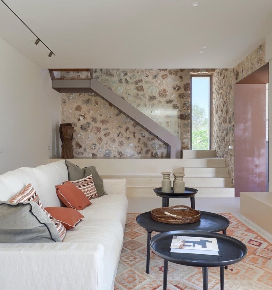 Interior view of a living room featuring a cream sofa, stone accent wall, inset fireplace, and floating staircase steps.