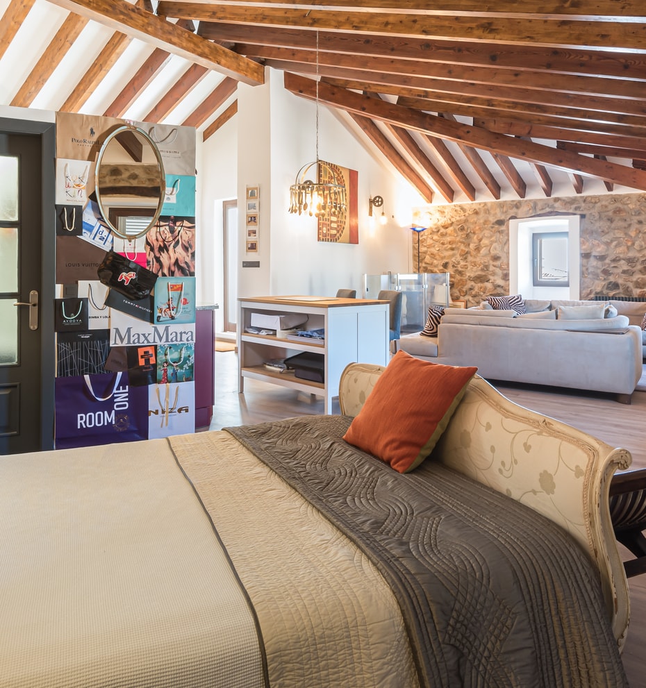 Loft-style bedroom featuring exposed wooden beams, stone walls, and an integrated living space.
