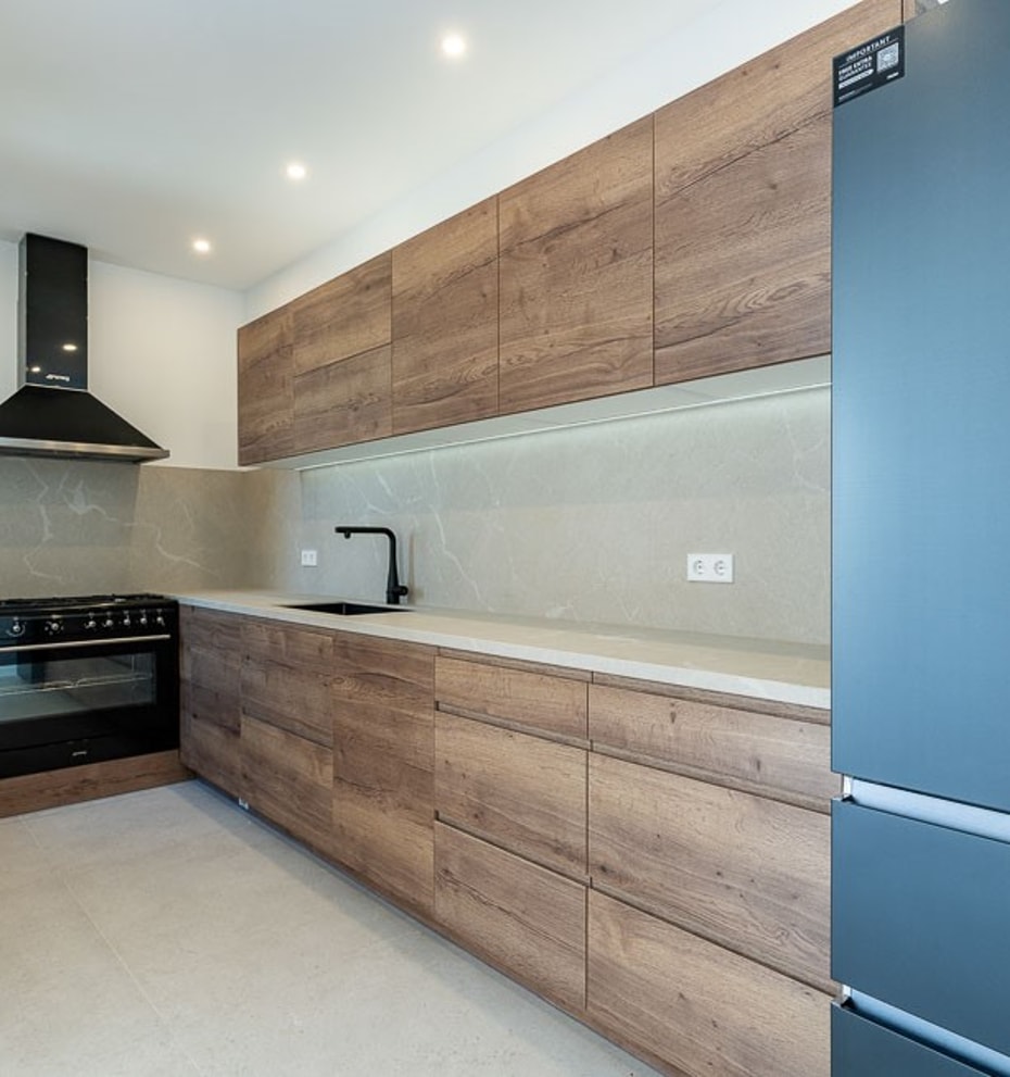A modern kitchen in a townhouse featuring wood grain cabinets, dark appliances, stone countertops, and recessed ceiling lights.