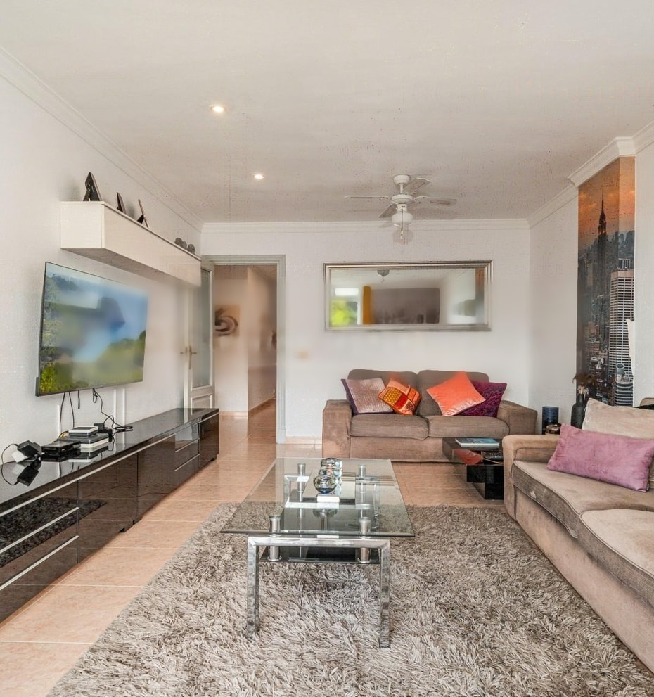 Living room featuring a brown sofa, glass coffee table, wall-mounted electric fireplace, and dark glossy media console.